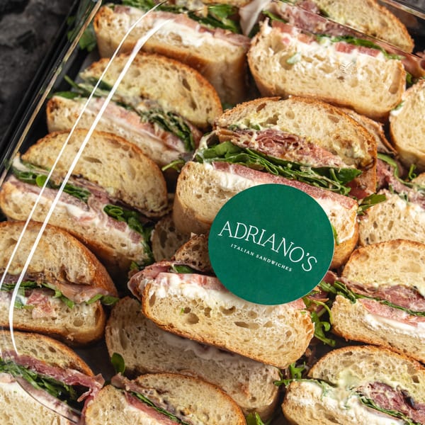 Close-up of Adriano's Italian sandwiches with prosciutto, arugula, and cheese on a platter.