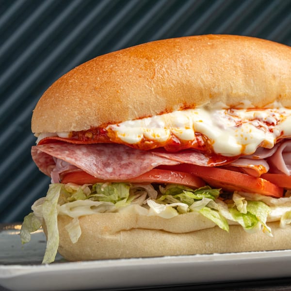 Close-up of a submarine sandwich with salami, ham, lettuce, tomato, and melted cheese.