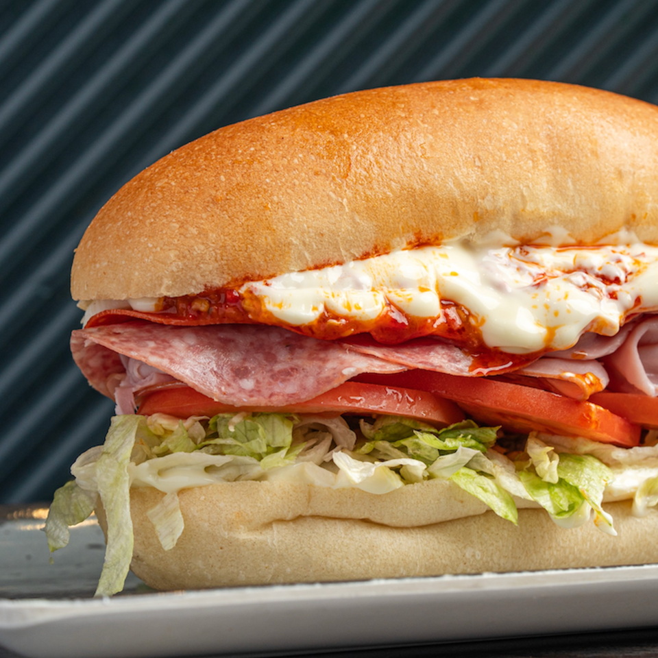 Close-up of a submarine sandwich with salami, ham, lettuce, tomato, and melted cheese.