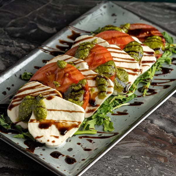 Caprese salad with sliced tomatoes, mozzarella, pesto, and balsamic glaze on a bed of arugula.