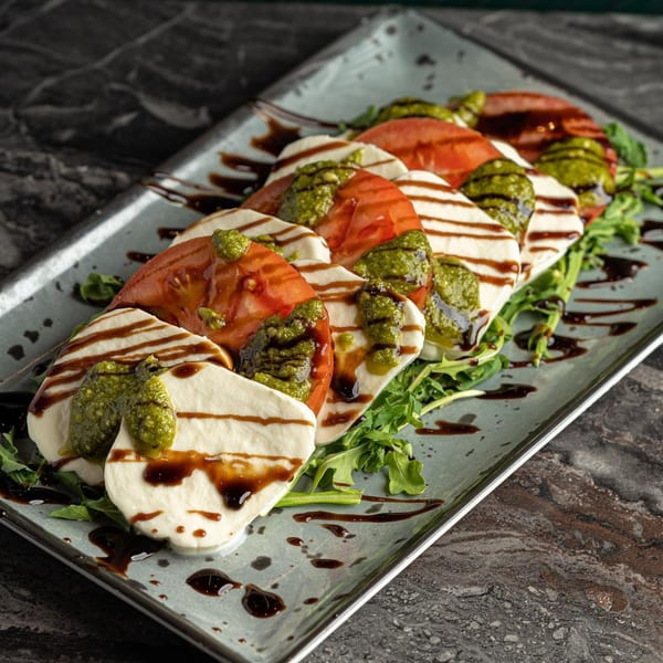 Caprese salad with sliced mozzarella, tomatoes, pesto, and balsamic glaze on a bed of arugula.