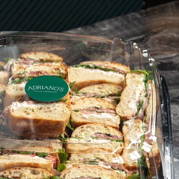 Adriano's Italian Sandwiches catering tray filled with many small sandwiches, each cut in half.