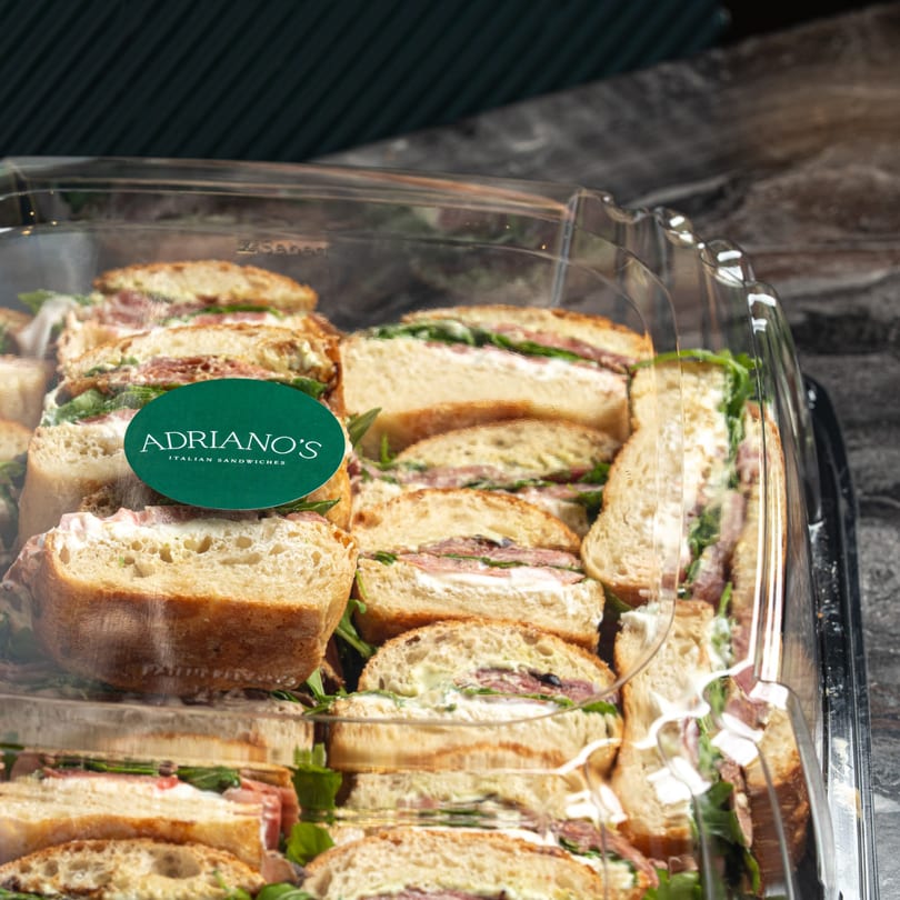 Adriano's Italian Sandwiches catering tray filled with many small sandwiches, each cut in half.