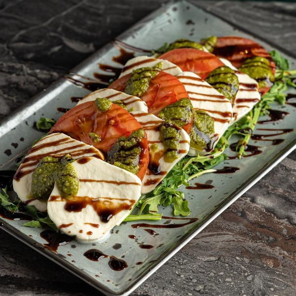 Caprese salad with sliced mozzarella, tomatoes, pesto, and balsamic glaze on a bed of arugula.