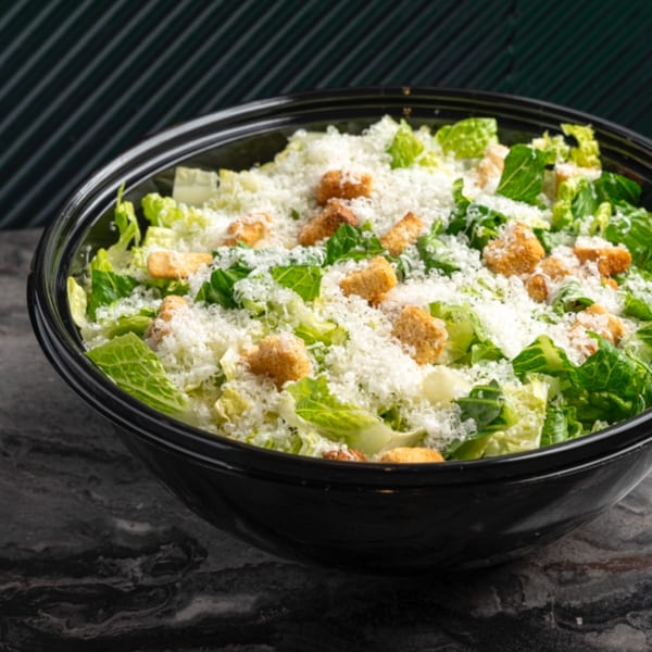 Caesar salad in a black bowl, topped with shredded cheese and croutons.