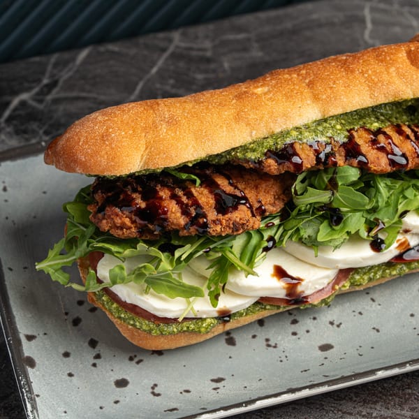 Crispy chicken cutlet sandwich with pesto, mozzarella, arugula, and balsamic glaze on a baguette.