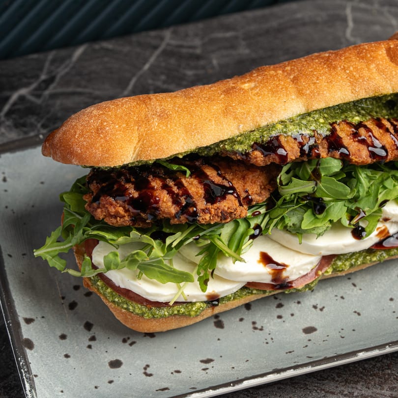 Crispy chicken cutlet sandwich with pesto, mozzarella, arugula, and balsamic glaze on a baguette.