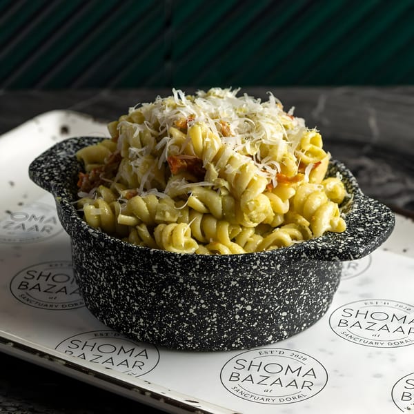 A black speckled bowl filled with pasta, topped with shredded cheese, on a branded paper liner.