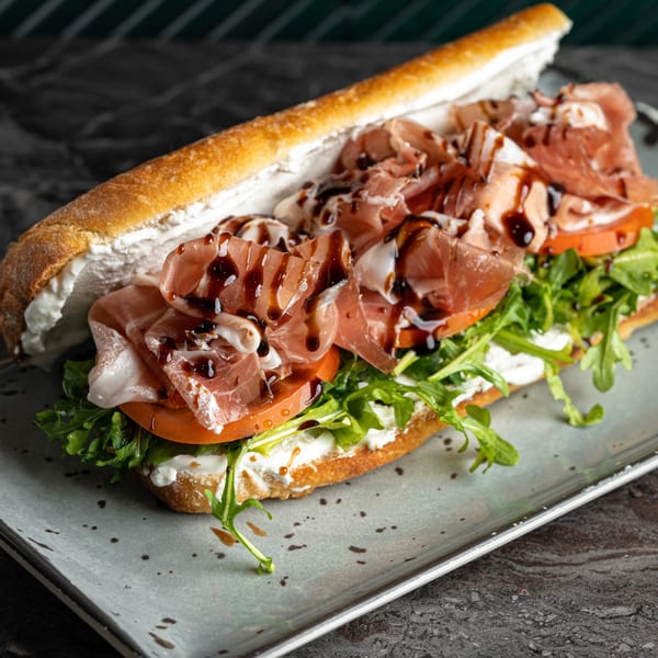 SNDWCH prosciutto sandwich with arugula, tomatoes, and balsamic glaze on a baguette.