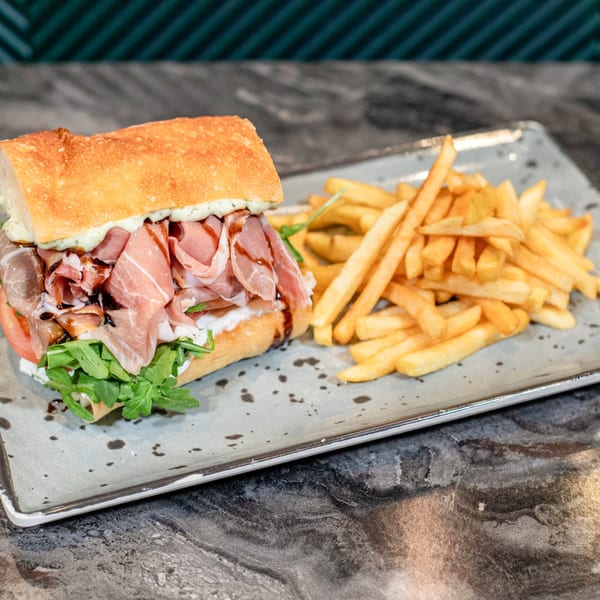 A SNDWCH prosciutto sandwich with arugula, tomato, and balsamic glaze, served with golden fries.