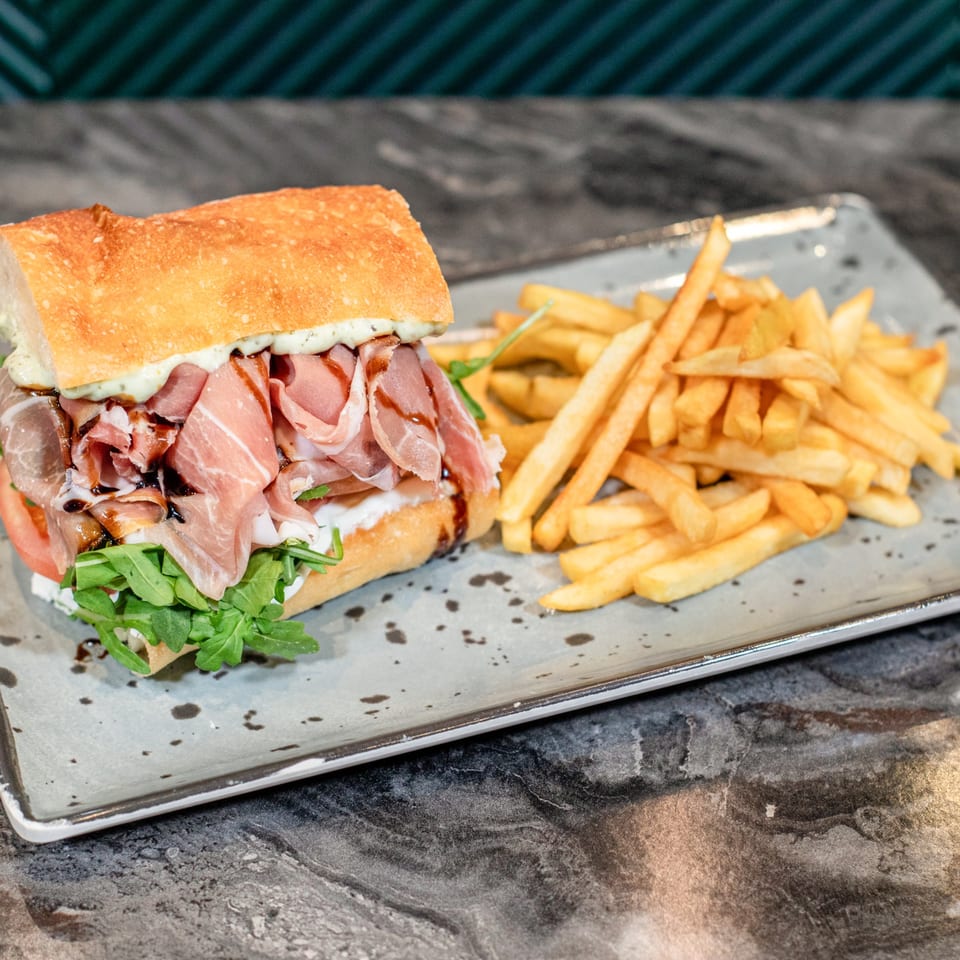 A SNDWCH prosciutto sandwich with arugula, tomato, and balsamic glaze, served with golden fries.