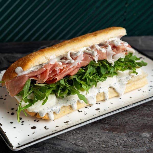 SNDWCH prosciutto sandwich with arugula, mozzarella, and creamy dressing on a baguette.