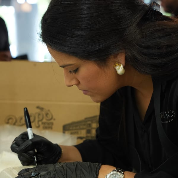 A woman in black gloves and shirt writes on a container with a marker.