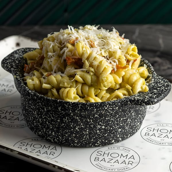 A black speckled bowl filled with pasta, topped with shredded cheese and red bits, on a branded tray.