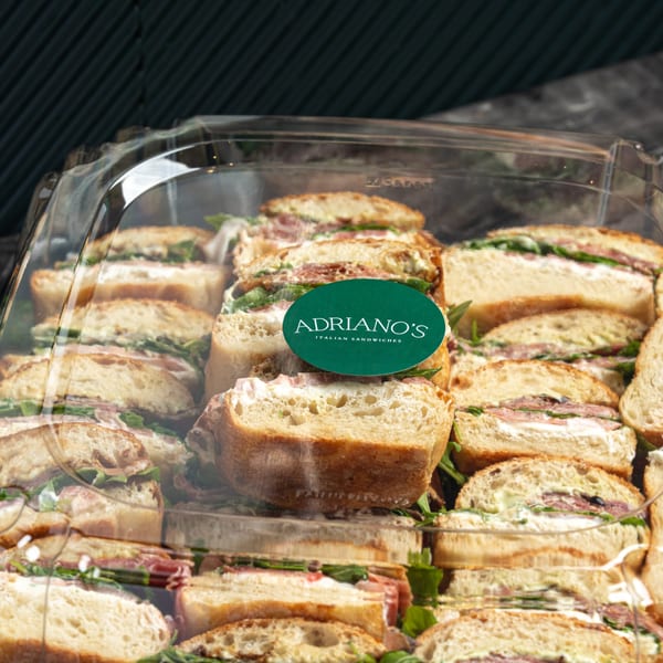 Adriano's Italian Sandwiches catering tray filled with sliced sandwiches, prosciutto, arugula, and cream cheese.