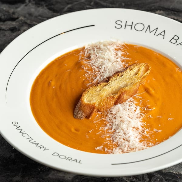 Orange tomato soup with a slice of toasted bread and shredded cheese in a white bowl.