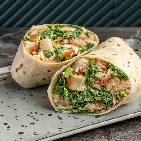 Two halves of a chicken Caesar salad wrap, filled with crispy chicken, lettuce, and dressing.